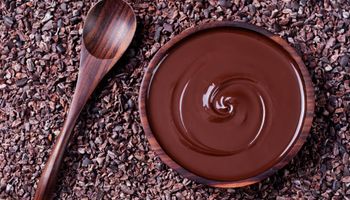 Löffel und eine Schale mit geschmolzener Schokolade auf Kakaobohnen.