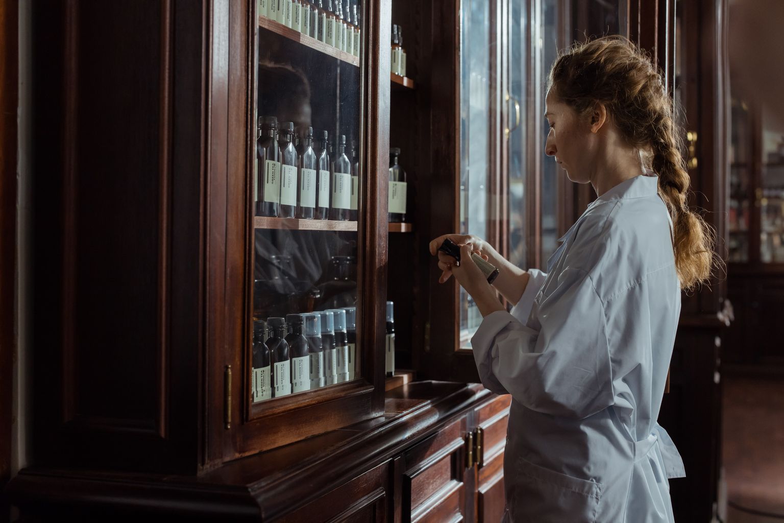 A mulher abre um armário de farmácia feito de madeira e vidro e inspecciona um medicamento.