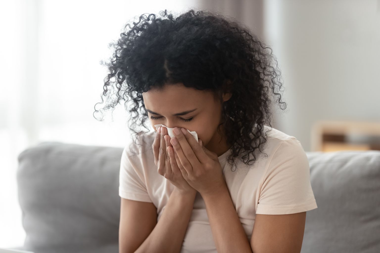 Mujer africana enferma y enfadada que se suena la nariz, tiene una gripe que se asienta en los pañuelos, mujer negra alérgica enferma con síntomas de alergia que tose una servilleta en casa, concepto de fiebre del heno