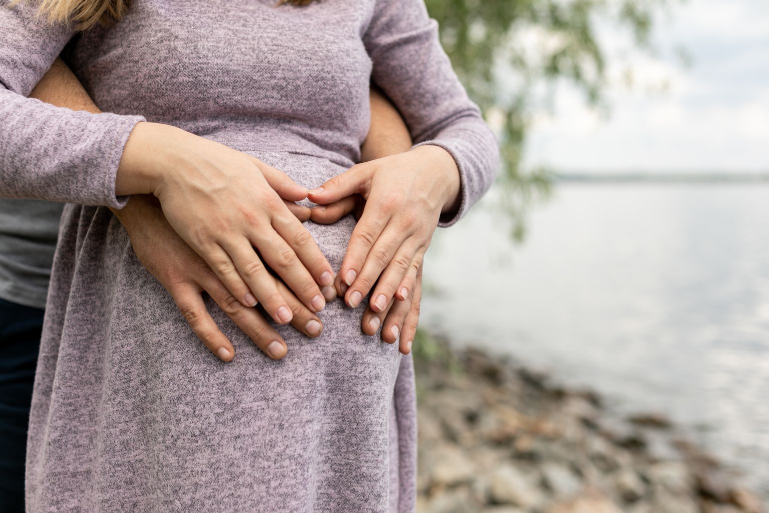 Pair of hands holding pregnant young women belly
