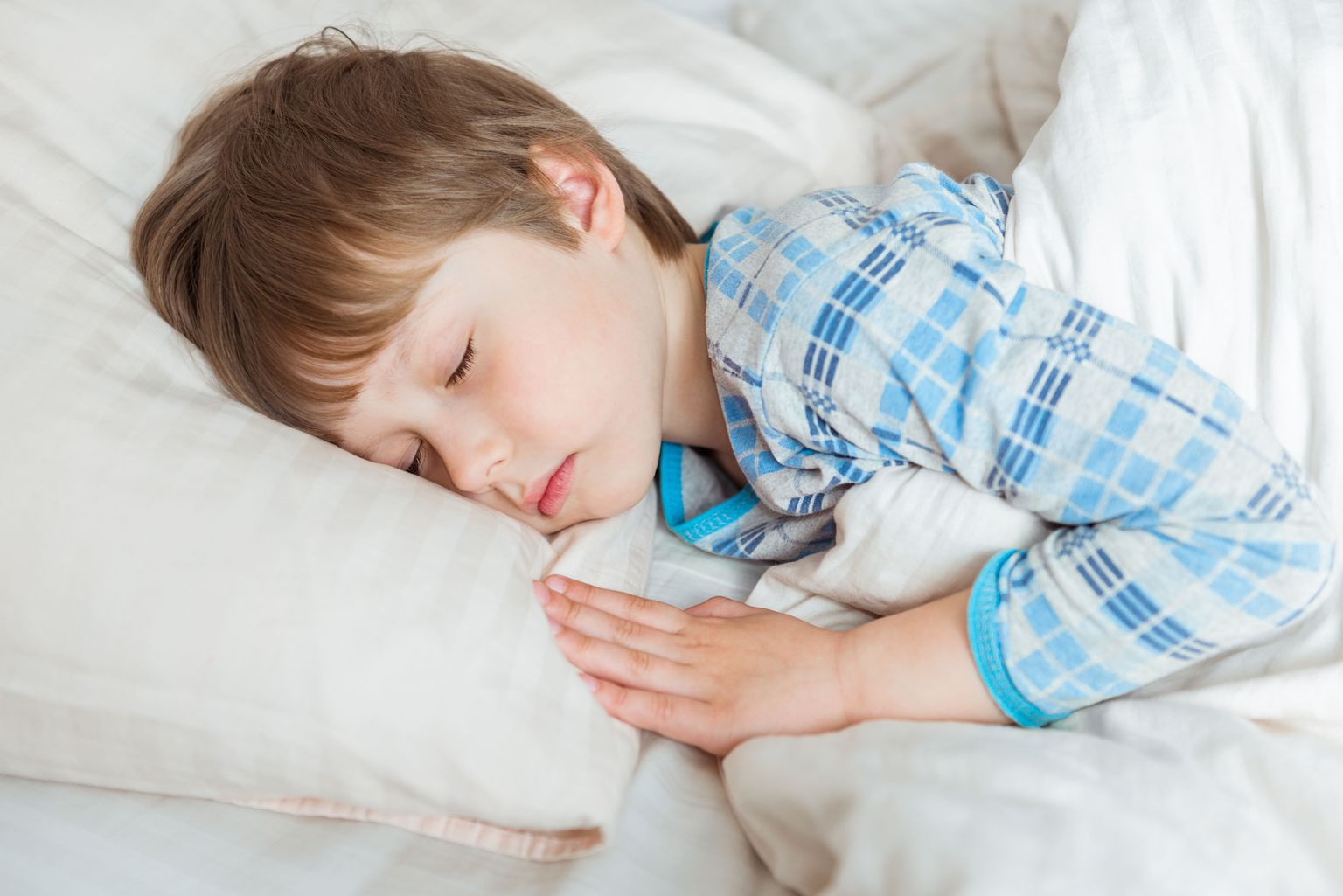 Um menino deitado na cama com os olhos fechados.