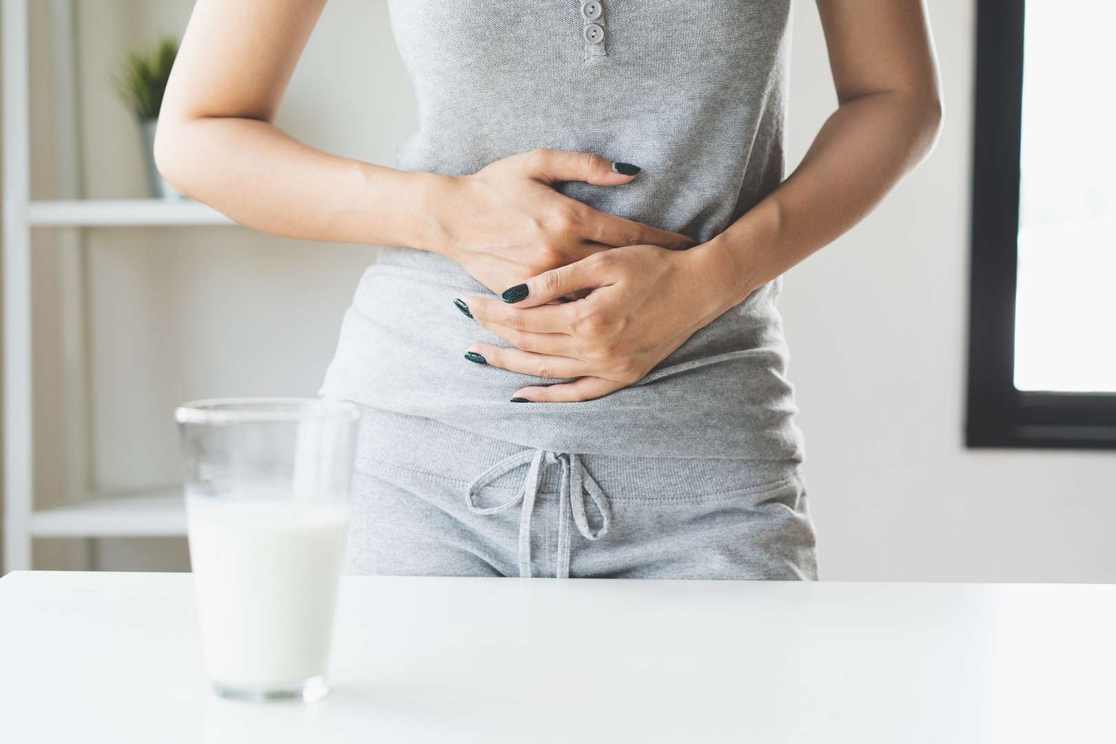 Vrouw houdt haar buik vast met beide handen. Op de voorgrond staat een glas met melk.