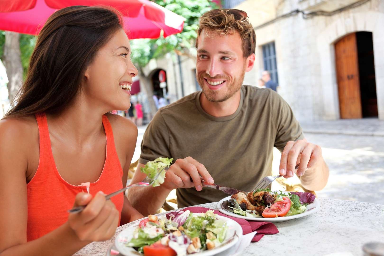 Twee mensen eten in een restaurant en glimlachen naar elkaar.