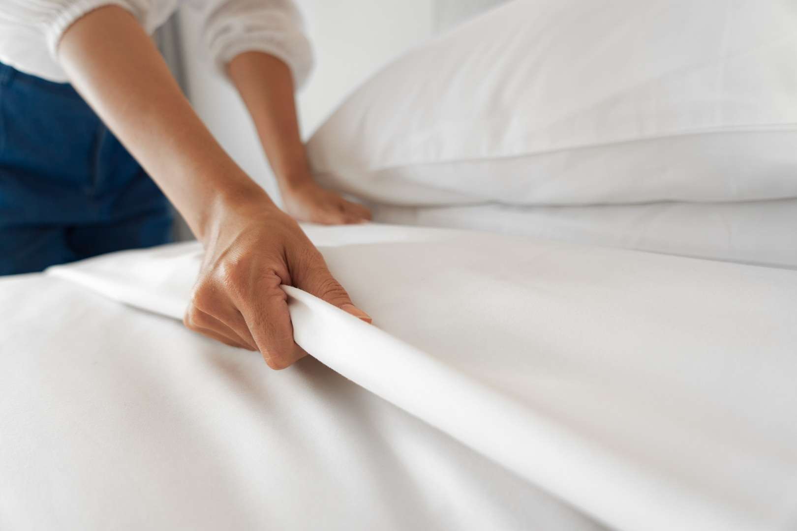 Een persoon bedekt een bed. Je ziet alleen de armen en een deel van het bed.