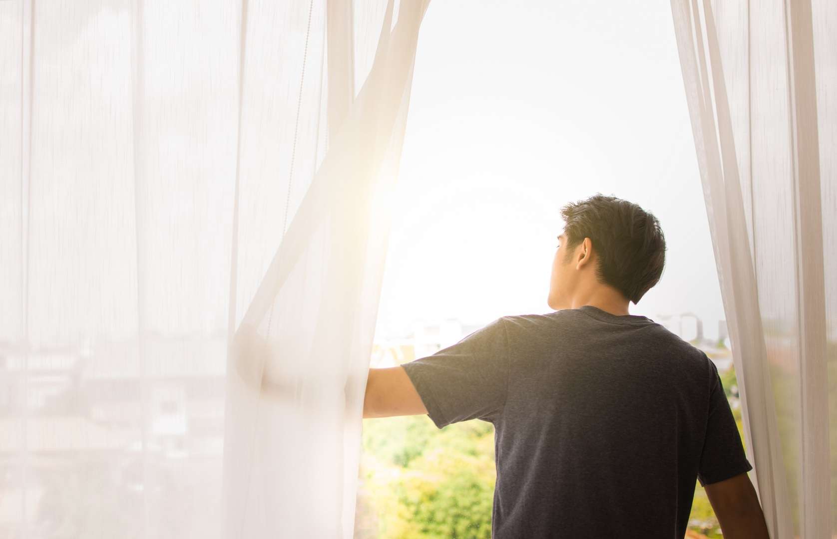 Eén persoon schuift een licht gordijn opzij, zodat de zon erdoor kan schijnen.
