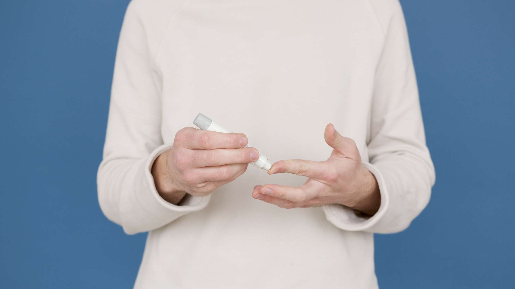Pexels/pexels-artem-podrez-6823571 Een vrolijk geklede persoon gebruikt een insulinepen, blauwe achtergrond.