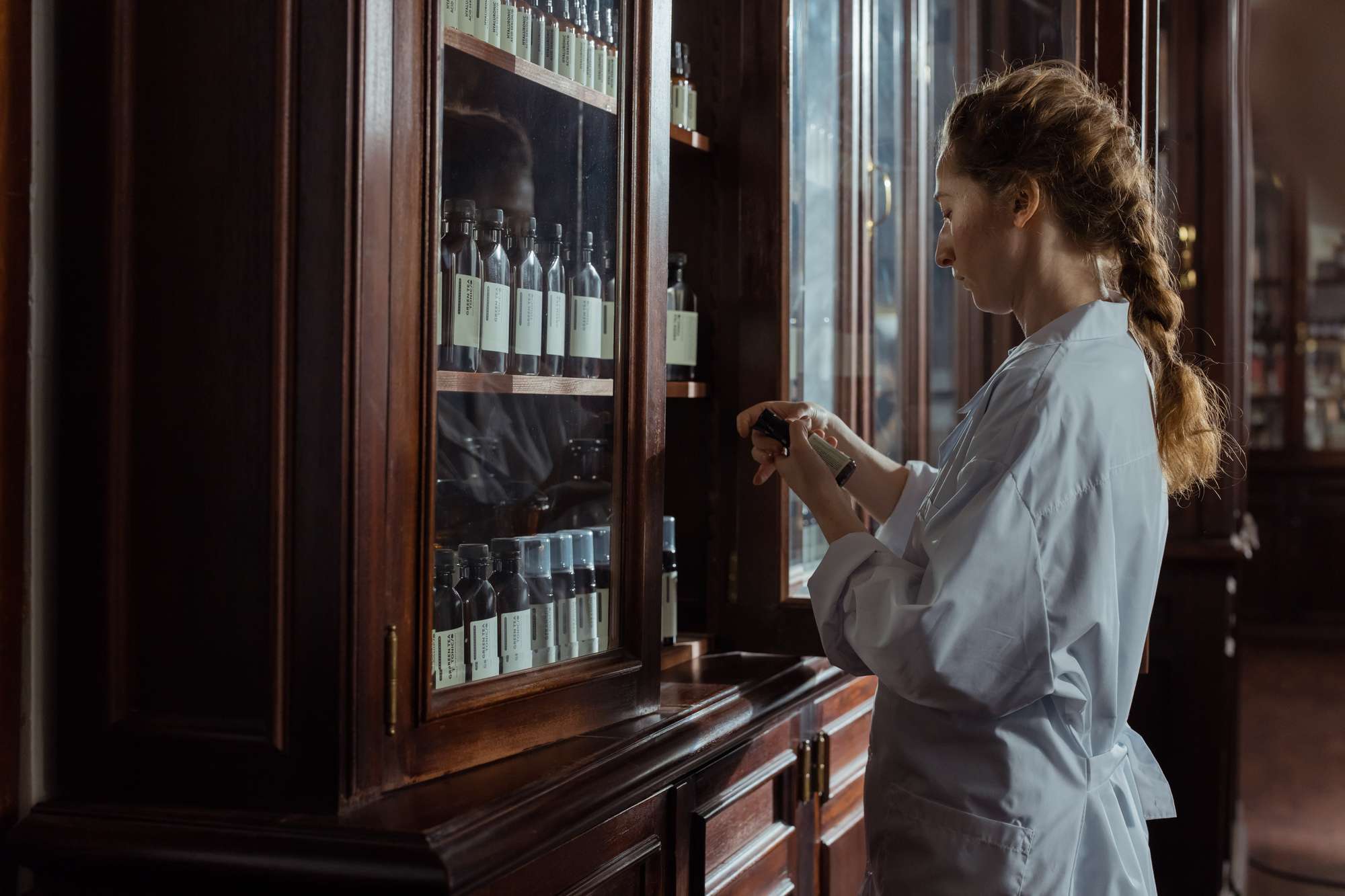 Pexels Vrouw opent een apothekerskast van hout en glas en inspecteert een geneesmiddel.