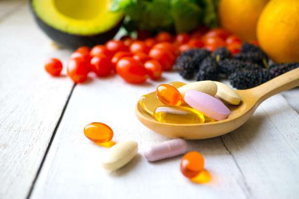 Pilules et gélules dans une cuillère en bois avec des fruits frais en arrière-plan. Pilules et gélules dans une cuillère en bois avec des fruits frais. Multivitamines et suppléments issus du concept des fruits.