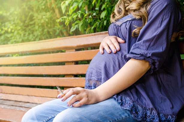 Gros plan de femme enceinte fumant une cigarette en plein air dans un parc sur fond naturel Habit interdit Une femme enceinte est assise sur un banc dans un parc et fume une cigarette.