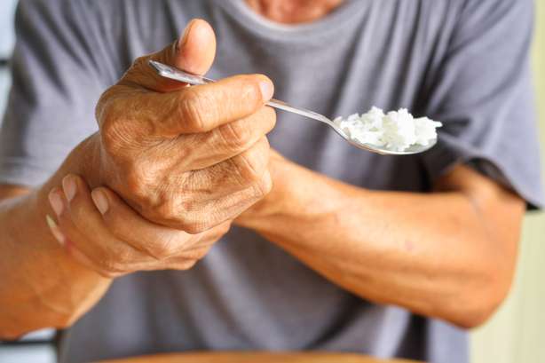 Ältere Menschen halten sich die Hand beim Essen, weil Parkinson's Krankheit. Tremor ist das beste Symptom und machen Schwierigkeiten für Aktivitäten wie Essen. Ein älterer Mensch haltet sich beim Essen die Hand.