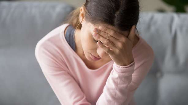 Junge Frau greift sich auf die Stirn. Junge müde ungesunde gemischte Rasse Frau sitzend auf Sofa im Wohnzimmer zu Hause mit geschlossenen Augen, halten Kopf mit der Hand, leiden an starken plötzlichen Kopfschmerzen oder Migräne, wirbelnden Schmerzen.