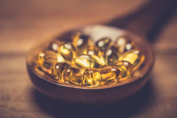 Capsules de gel d'oméga-3 d'huile de foie de cod, isolées sur fond de bois. Gélules de vitamine D. Complément alimentaire Des capsules de vitamine D dans une cuillère en bois sur une table en bois.