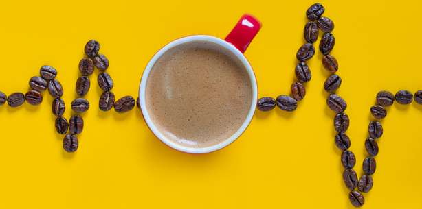 Pulslinie aus Kaffeebohnen mit roter Kaffeetasse auf gelbem Hintergrund. Herzschlag Pulslinie mit roter Kaffeetasse auf gelbem Hintergrund. Kaffee Cardio Images.Kaffee Herz