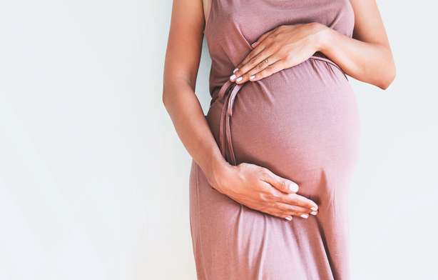 Femme enceinte en vêtements tenant les mains sur le ventre sur fond blanc. Concept de grossesse, de maternité, de préparation et d'attente. Gros plan, salle de photocopie, intérieur. Belle image d'ambiance délicate de la grossesse. Une femme enceinte tient son ventre. Le fond est blanc.