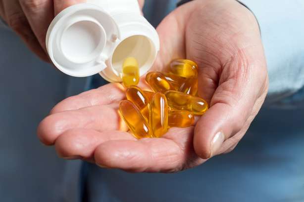 Eine Person haltet mehrere Omega-3-Kapseln in der linken Hand. Die weibliche Hand hält gelbe Medikamentenkapseln von Omega 3, Griechen aus einer weißen Flasche in Palme das Fischöl, gesunde Beipackzettel.