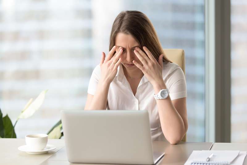 Een zakenvrouw op haar werkplek masseert haar oogleden om te ontspannen.