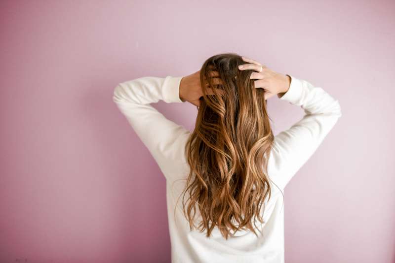 Mulher com camisa branca de manga comprida Uma mulher com uma camisa branca agarra o seu cabelo e fica de costas para a câmara.