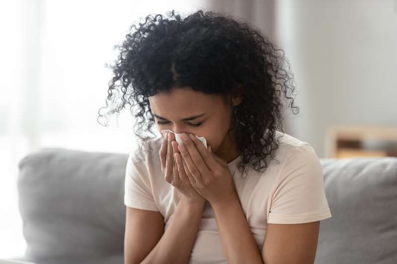 Zieke boze Afrikaanse vrouw snuit loopneus, kreeg griep die zich in weefsels nestelde, zieke allergische zwarte vrouw met allergische symptomen hoest thuis een servet uit, hooikoortsconcept